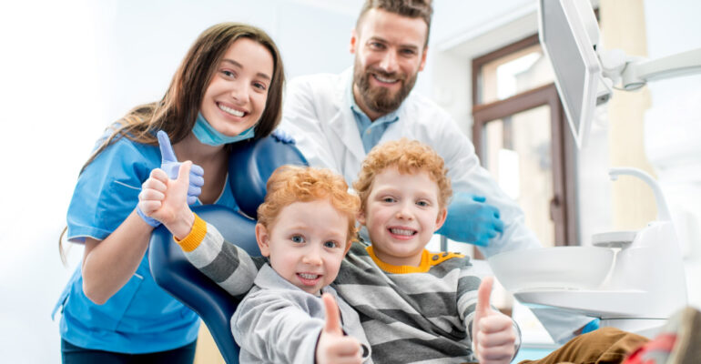 portret szczęśliwych młodych chłopców siedzących na krześle z dentysta i asystentka w gabinecie stomatologicznym